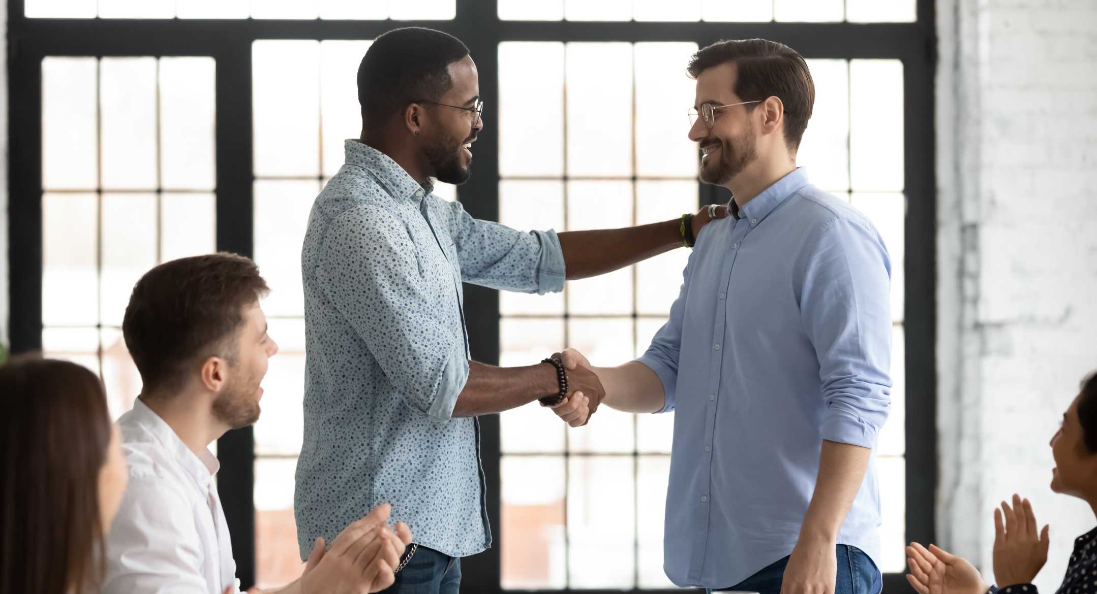 Two men shaking hands and others clapping