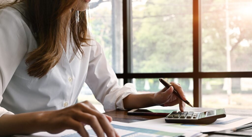 A woman at a desk using a calculator and reviewing costs and profits