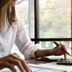 A woman at a desk using a calculator and reviewing costs and profits