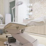 A dermatology office with a white and clean aethetic, focusing on the chair, medical equipment, and products.
