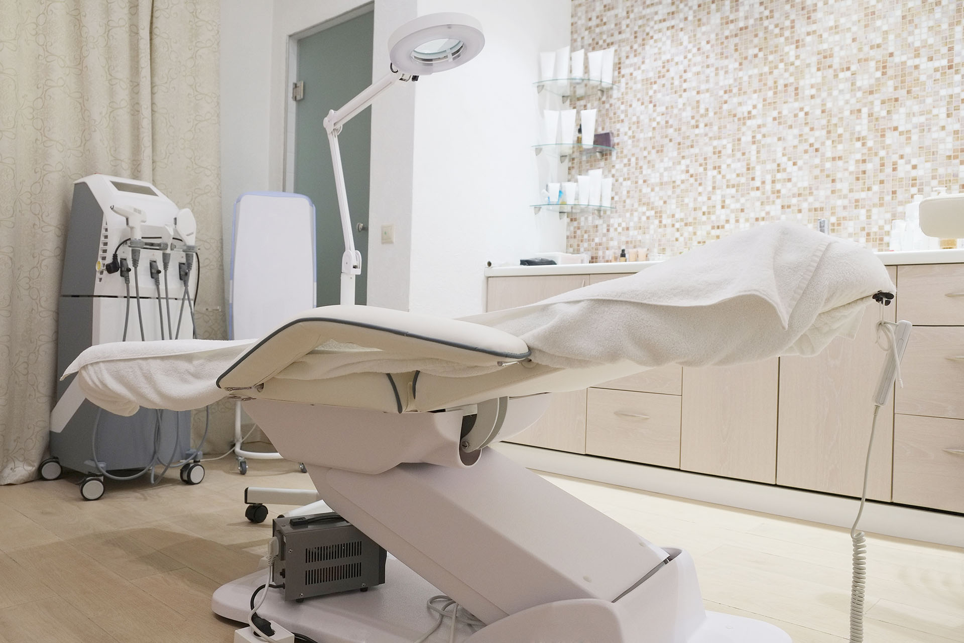 A dermatology office with a white and clean aethetic, focusing on the chair, medical equipment, and products.