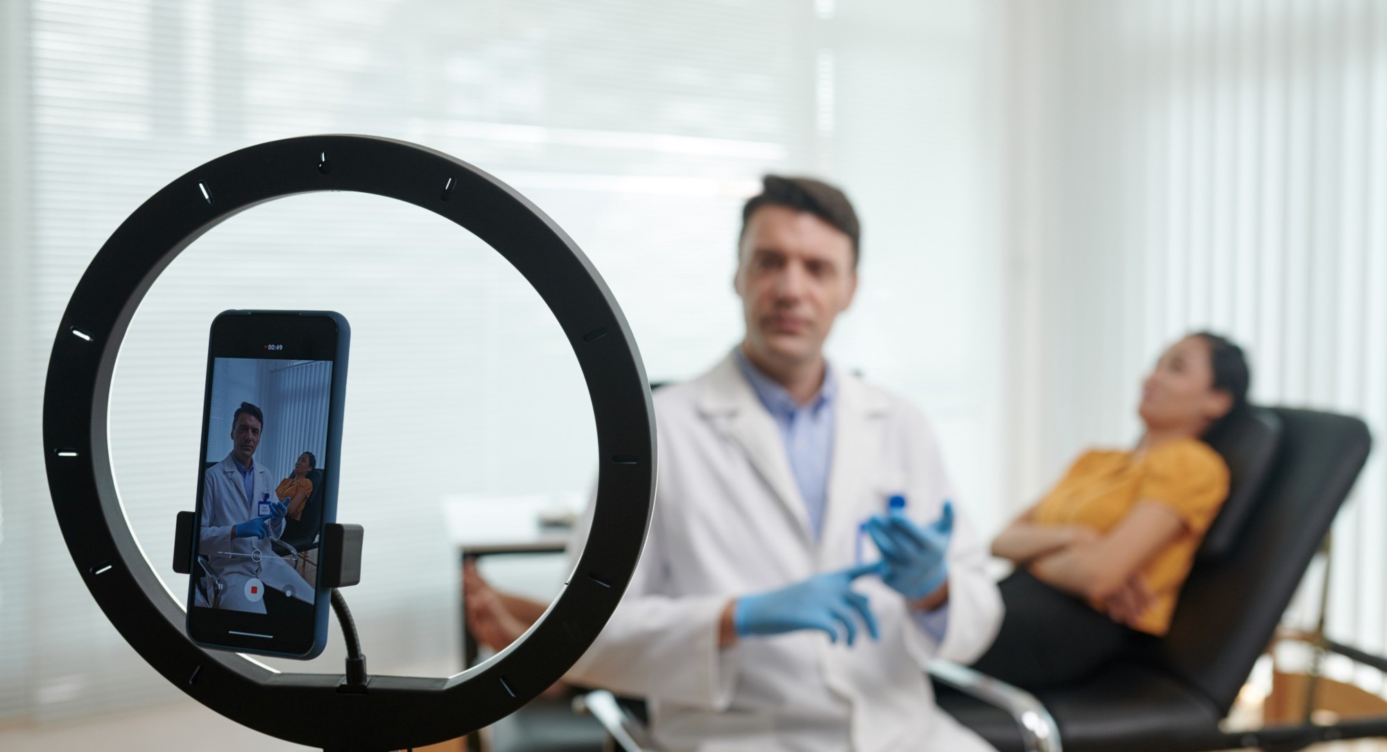 A physician films a video in clinic with a smartphone mounted in a ring light